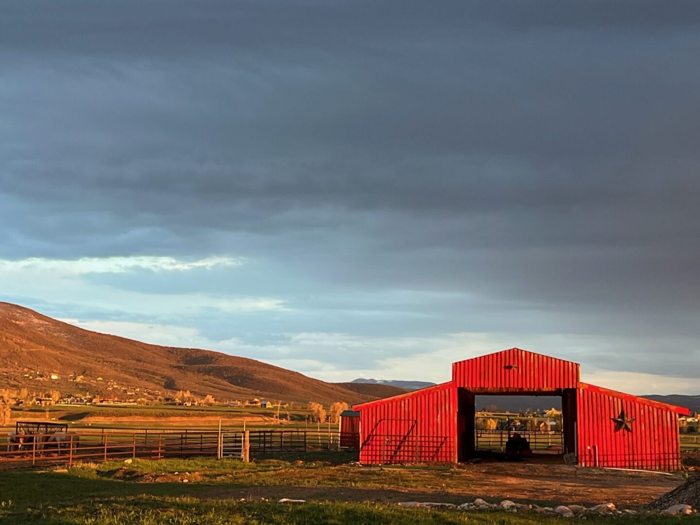 A red barn sits in the middle of a field with mountains in the background.