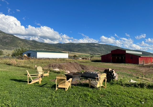 A red barn with chairs and a fire pit in the middle of a grassy field.