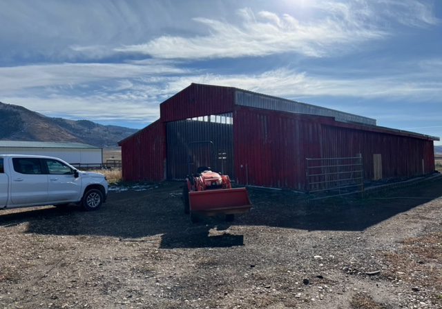 A truck is parked in front of a red barn.